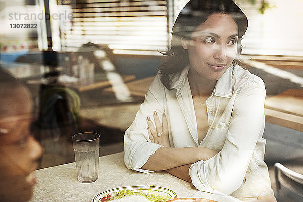 Frau schaut weg  während sie mit einem Freund im Restaurant sitzt und durch ein Fenster gesehen wird