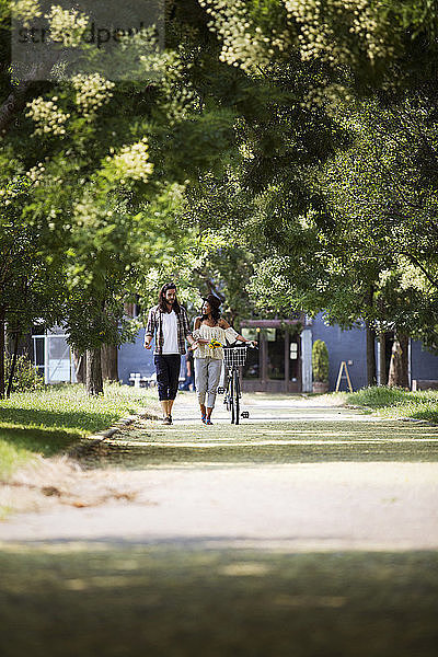 Paar unterhält sich beim Spaziergang mit dem Fahrrad auf dem Fußweg im Park