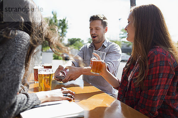 Glückliche Freunde trinken Bier beim Kartenspielen am Tisch in einer Brauerei