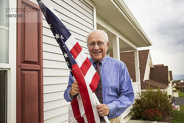 Porträt eines älteren Mannes  der die amerikanische Flagge hält  während er gegen das Haus steht