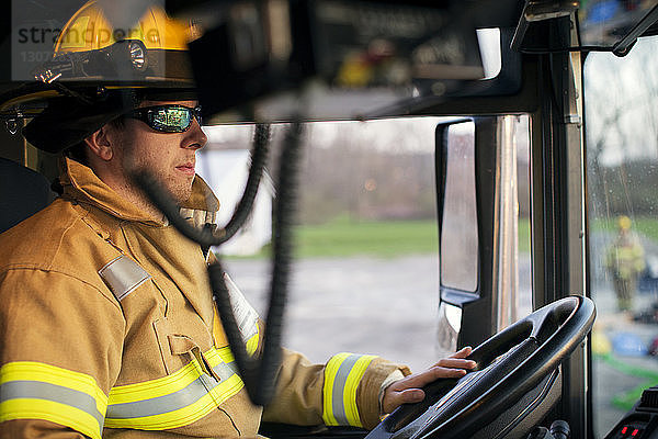 Selbstbewusster Feuerwehrmann schaut weg  während er im Feuerwehrauto sitzt