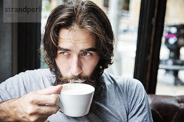 Nahaufnahme eines Mannes mit Bart  der Kaffee trinkt  während er im Café sitzt