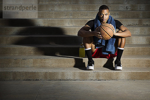 Porträt eines Sportlers mit Basketball auf Stufen sitzend