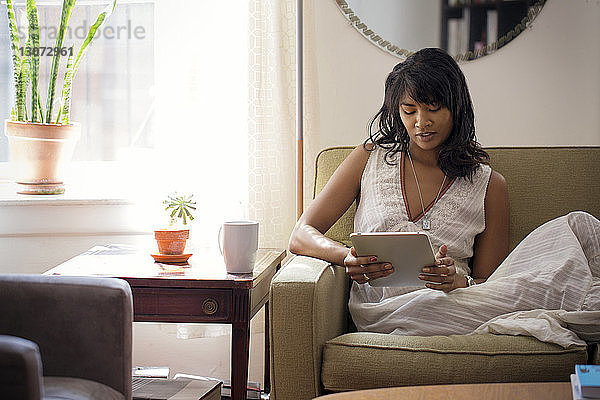 Frau benutzt Tablet-Computer  während sie sich zu Hause auf dem Sofa entspannt