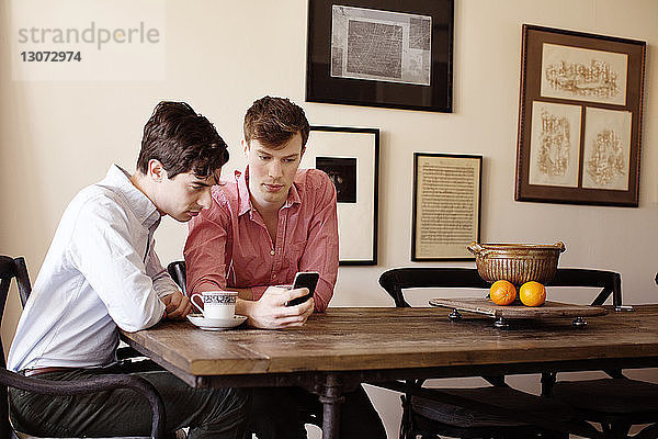 Schwule Männer  die am Tisch sitzend auf ein Smartphone schauen