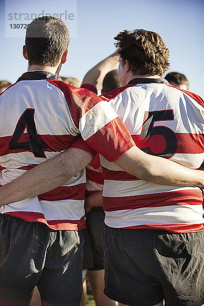 Rückansicht von Rugby-Spielern  die Arm in Arm gegen den Himmel stehen