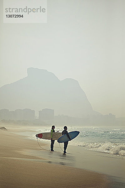 Paar  das Surfbretter trägt  während es am Strand auf Sand steht