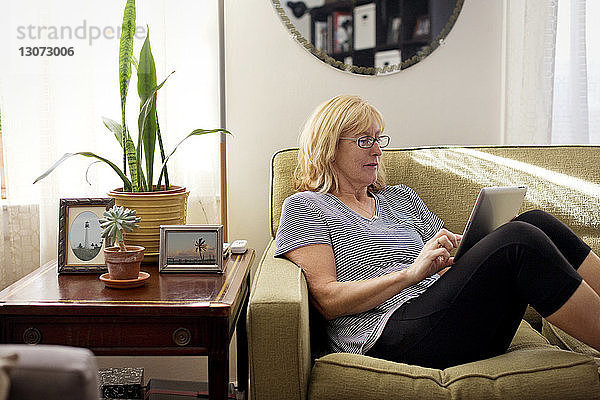 Frau benutzt Tablet-Computer  während sie zu Hause auf dem Sofa sitzt