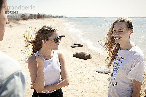 Freunde unterhalten sich  während sie am Strand an der Küste stehen