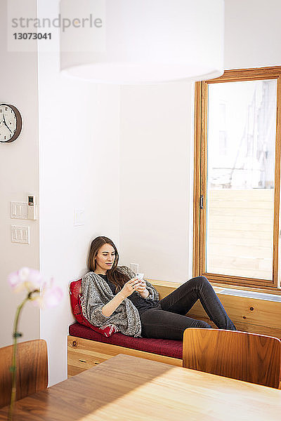 Frau benutzt Mobiltelefon  während sie zu Hause auf dem Sofa liegt