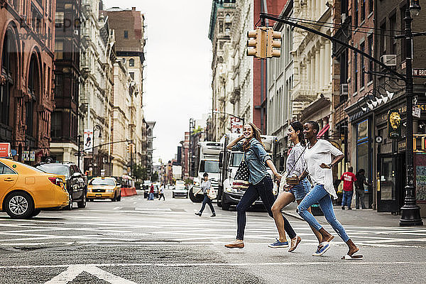 Lächelnde Freunde rennen beim Überqueren der Straße in der Stadt