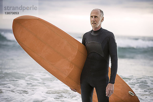 Älterer Mann mit Surfbrett schaut weg  während er im Meer steht