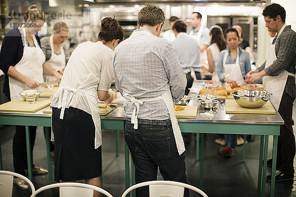 Schüler  die an Tischen Essen zubereiten  während sie in einer Großküche stehen