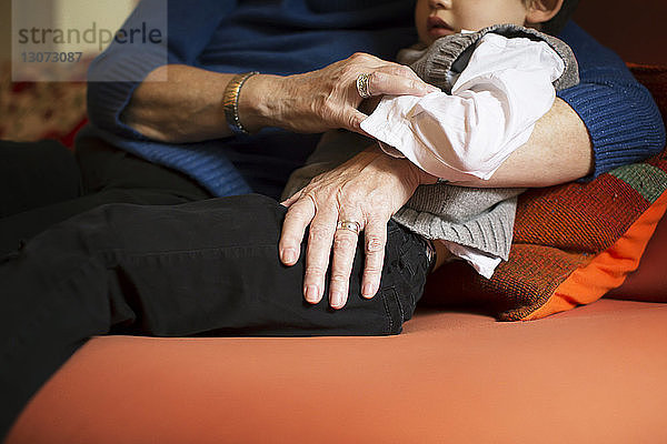 Mitschnitt der Großmutter  die den Jungen umarmt  während sie sich zu Hause auf dem Sofa entspannt