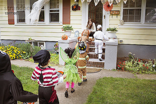 Kinder in Halloween-Kostümen gehen während eines Streichs oder einer Behandlung auf die Frau zu