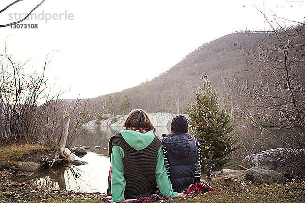Freunde sitzen auf einem Handtuch am Seeufer am Weihnachtsbaum