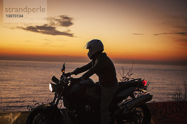 Mann fährt Motorrad am Meer gegen den Himmel bei Sonnenuntergang