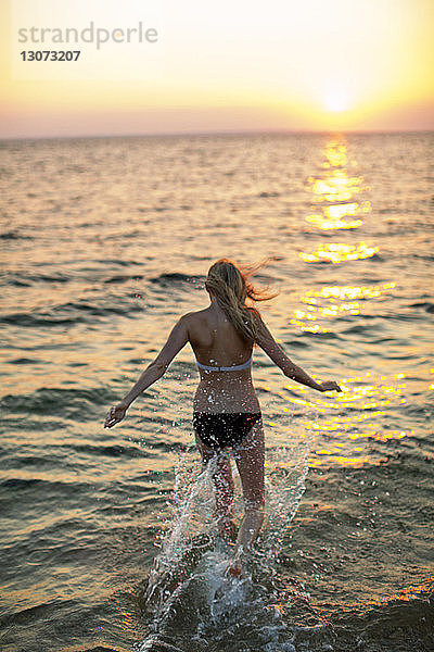 Rückansicht einer Frau  die bei Sonnenuntergang am Strand an der Küste läuft
