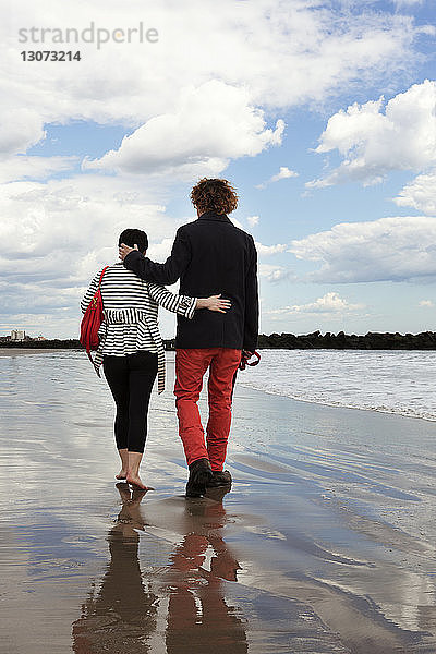 Paar spricht beim Strandspaziergang gegen bewölkten Himmel