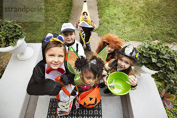 Fröhliche Kinder in Halloween-Kostümen  die während einer Süßes-oder-Saures-Tour vor der Tür stehen