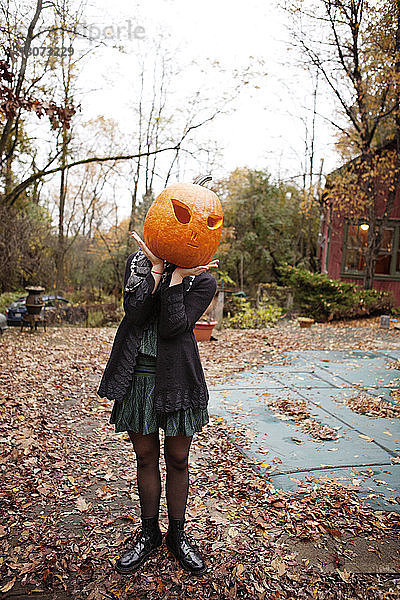 Frau versteckt Gesicht mit Halloween-Kürbis  während sie auf dem Feld steht