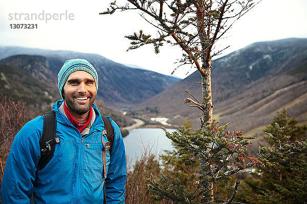 Porträt eines lächelnden Wanderers  der an einem Baum vor den Bergen steht