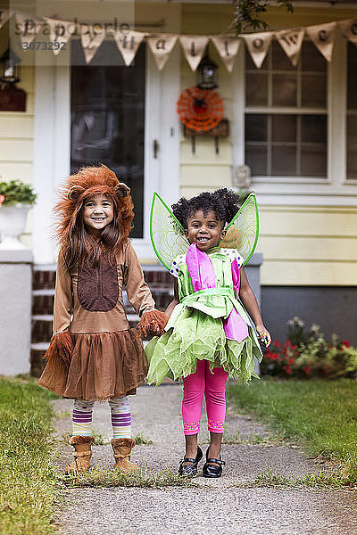 Porträt von lächelnden Mädchen in Halloween-Kostüm  die vor dem Haus im Hof stehen