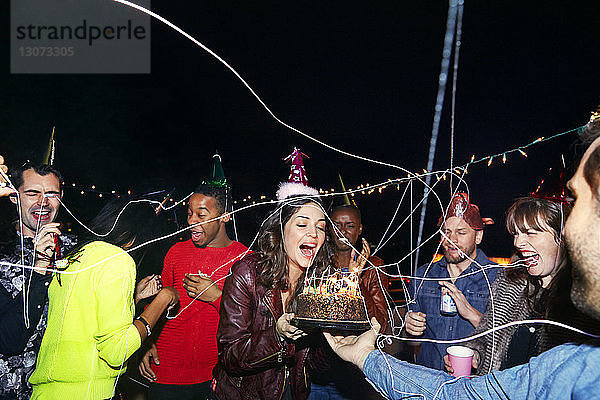Glückliche Freunde genießen mit Geburtstagskuchen in nächtlicher Party