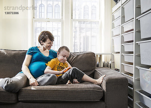 Schwangere Frau mit Sohn sitzt zu Hause auf dem Sofa