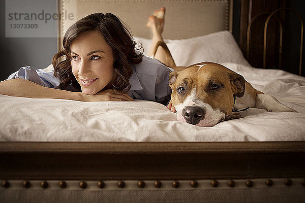 Frau schaut weg  während sie sich zu Hause mit Hund im Bett entspannt