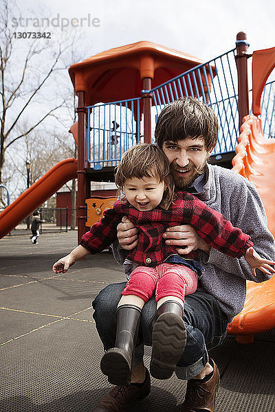 Porträt eines Mannes mit Tochter am Spielplatz kauernd