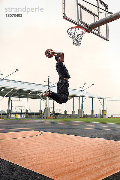 Seitenansicht eines Mannes  der beim Üben von Basketball vor Gericht gegen den Himmel punktet