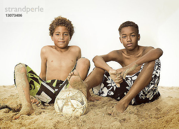 Porträt von Jungen  die auf Sand vor klarem Himmel sitzen