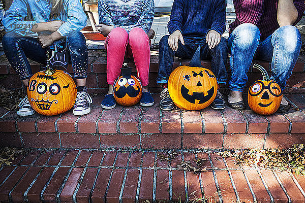 Niedriger Teil der Familie sitzt an Halloween mit dekorierten Kürbissen auf der Treppe