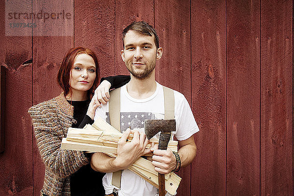 Porträt eines Mannes  der Brennholz und Axt hält  während er neben einer Frau steht