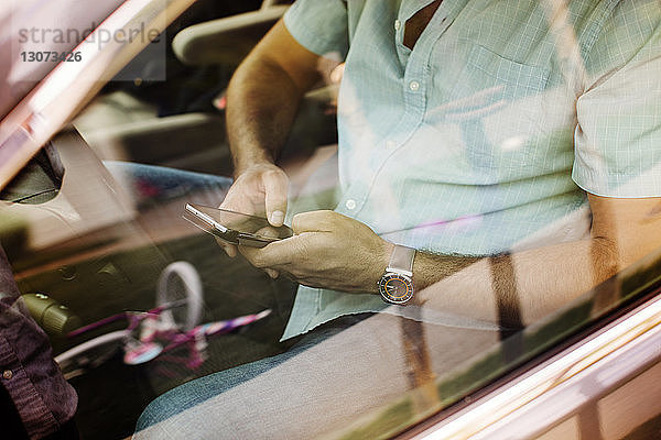 Hochwinkelansicht eines Mannes  der ein Smartphone benutzt  während er im Auto unterwegs ist  durch ein Fenster gesehen