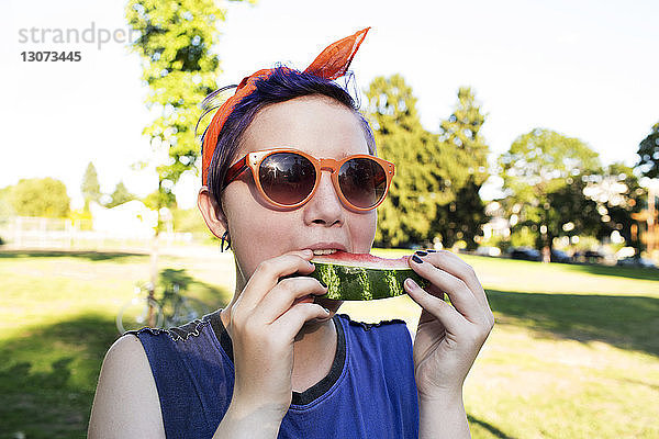 Teenager isst Wassermelone  während er an einem sonnigen Tag im Park steht
