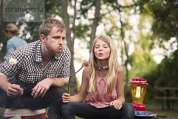 Vater und Tochter blasen beim Camping gebratene Marshmallows an