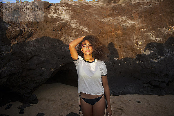 Porträt eines Teenagers  der an einem sonnigen Tag am Strand gegen einen Felsen steht