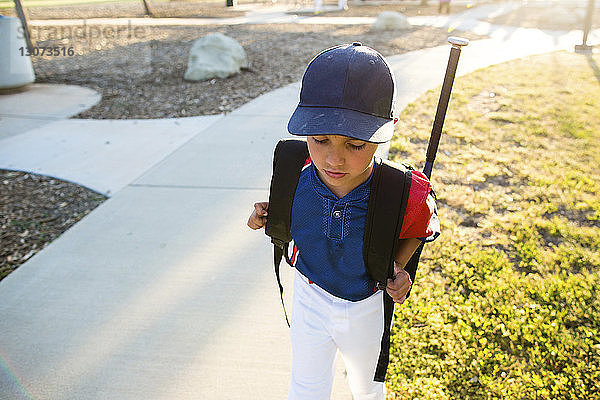 Hochwinkelaufnahme eines Jungen in Baseballuniform mit Rucksack  der im Hof geht