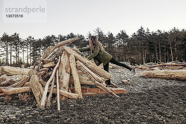 Seitenansicht einer Frau  die im Winter Brennholz am Strand arrangiert