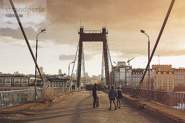 Freunde gehen bei Sonnenuntergang auf der Brücke gegen bewölkten Himmel