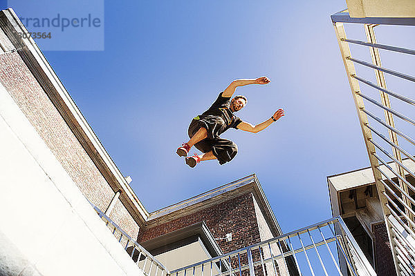 Niedrigwinkel-Ansicht eines Mannes  der bei klarem blauen Himmel auf Gebäude springt