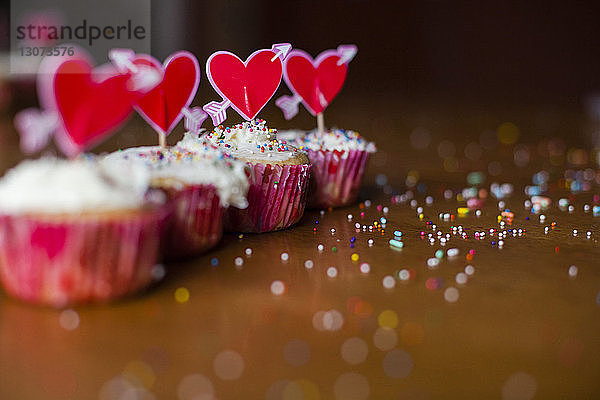 Mit herzförmigen Stäbchen verzierte Cupcakes auf Holztisch