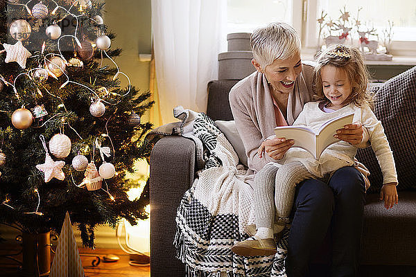 Großmutter und Mädchen lesen Buch  während sie zu Hause auf dem Sofa sitzen