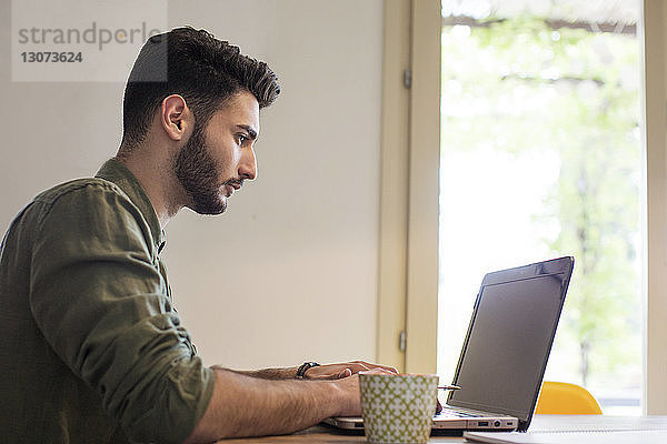 Seitenansicht eines Mannes mit Laptop am Tisch am Fenster