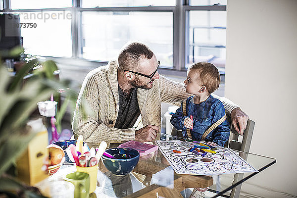 Lächelnder Vater malt mit der Tochter bei Tisch im hell erleuchteten Wohnzimmer
