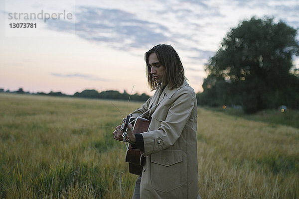 Seitenansicht eines Mannes  der Gitarre spielt  während er auf einem Grasfeld gegen den Himmel steht