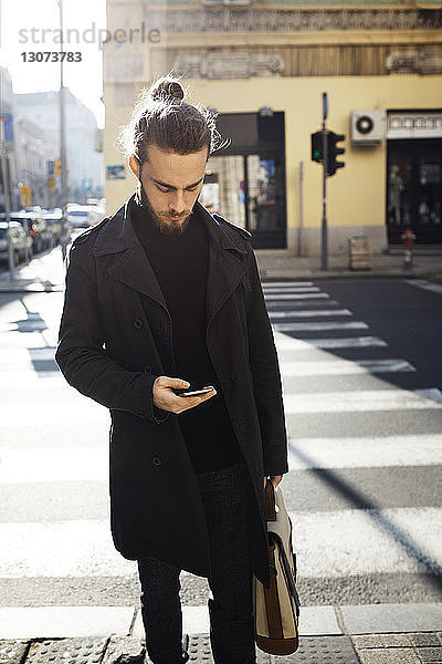 Mann benutzt Mobiltelefon  während er auf der Straße in der Stadt steht