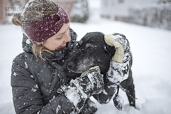 Glückliche Frau spielt mit Hund im Schnee
